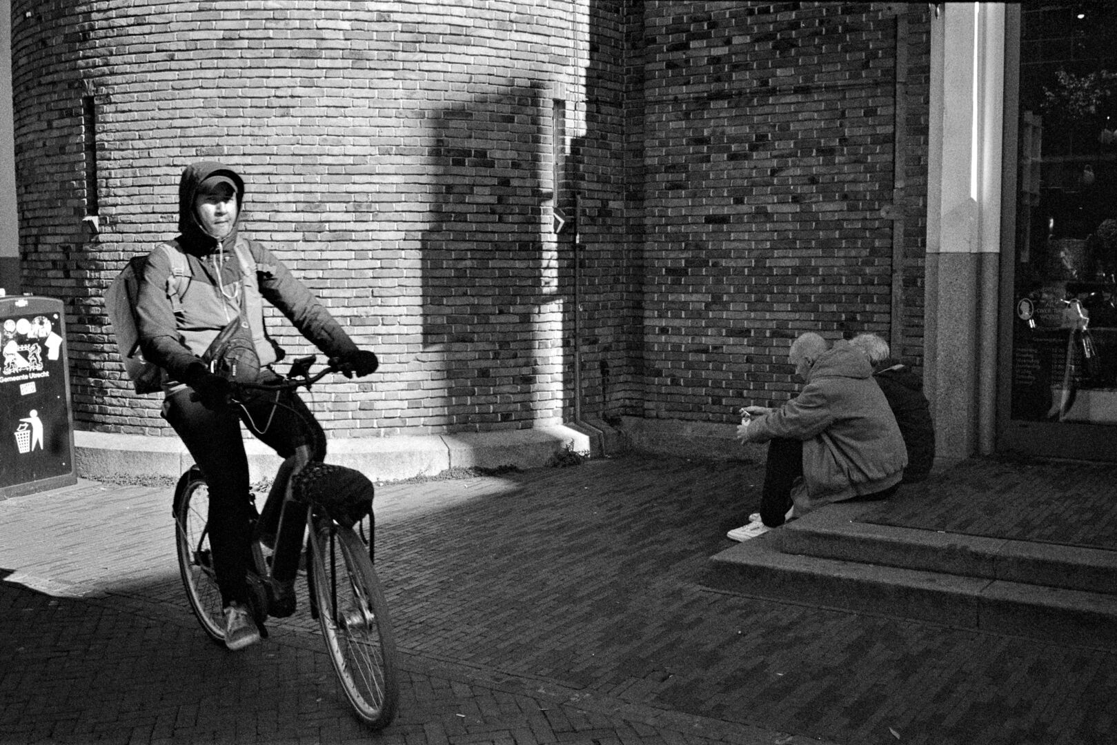 2024-10-09 street photography Utrecht Man on bicycle and two people sitting